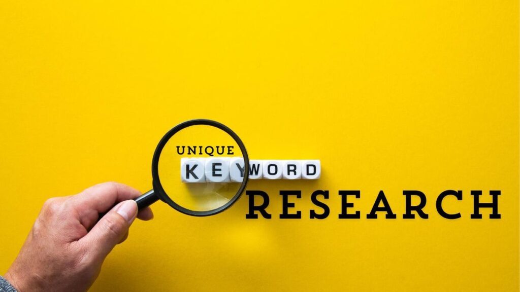 A hand holding a magnifying glass over white lettered blocks that spell out "KEYWORD," with the word "UNIQUE" printed above them and "RESEARCH" printed to the right, all set against a solid yellow background